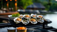 Fresh oysters grilled with savory toppings served on black slate plate at waterfront restaurant, garnished with herbs and accompanied by spicy sauce.