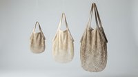 Three natural cotton mesh net bags in different sizes hanging against a neutral background, eco-friendly reusable shopping tote set.