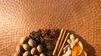 Warm spices including star anise, cinnamon sticks, nutmeg, almonds and dried citrus arranged on textured orange background for culinary, food styling and recipe content.