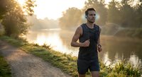 Young athletic Caucasian man jogging along peaceful river path during golden hour sunrise workout session for healthy active lifestyle and fitness motivation.