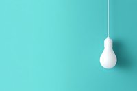 White lightbulb hanging on cord against turquoise wall background with copy space, minimalist creative concept for innovation and bright ideas.