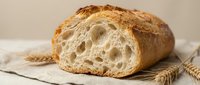 Freshly baked artisan bread loaf with golden crust and airy crumb structure on linen cloth with wheat stalks for bakery and food photography.
