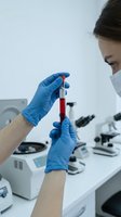 Female scientist examining blood sample in test tube wearing protective gloves and mask in modern laboratory for medical research and analysis.