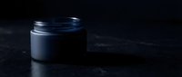 Dark matte cosmetic jar with open lid on black stone surface, moody luxury skincare product mockup for branding and packaging design.
