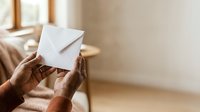 Close-up of mature hands holding blank white envelope indoors. Suitable for mail, correspondence, messaging, communication, and business concepts.
