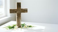 Rustic wooden cross with fresh white flowers on clean surface near window, symbolizing faith, hope, and spiritual devotion in peaceful setting.