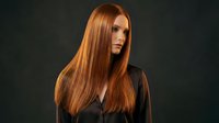 Young Caucasian woman with long straight red hair wearing black outfit against dark background for fashion and beauty concepts.