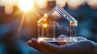 Transparent glass house model held in hand against sunset backdrop, symbolizing real estate investment, home ownership, and property dreams.