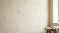 Cracked weathered wall texture with peeling paint in minimalist interior space with natural window light and wooden stool for rustic design projects.