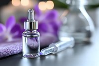 Luxury skincare serum bottle with dropper on spa table with purple orchid flowers and towel. Premium beauty treatment and wellness concept.
