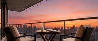 Luxury high-rise balcony with modern seating overlooking city skyline at sunset, golden hour urban landscape for hospitality and real estate marketing.