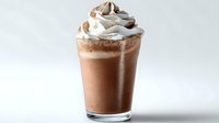 Refreshing chocolate milkshake topped with swirls of whipped cream and chocolate sprinkles in a clear glass against light background.