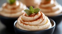 Creamy dessert swirls topped with fresh mint leaves and caramel drizzle in dark bowls, macro food photography showing texture and garnish details.