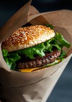 Juicy cheeseburger with beef patty, melted cheese and fresh lettuce in sesame bun, wrapped in craft paper. Dark moody background with dramatic lighting.
