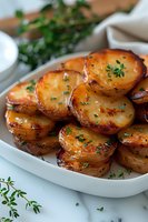 Crispy roasted potato slices garnished with fresh herbs and seasonings served on white plate, close-up view showing golden-brown caramelized edges and tender interior.