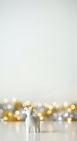 White ceramic llama figurine standing alone against soft bokeh background with warm gold and silver lights, suitable for holiday greeting cards, festive marketing materials, and seasonal promotional designs.