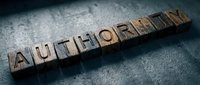 Wooden letter blocks spelling AUTHORITY on textured dark surface. Business leadership concept for corporate presentations and professional content.