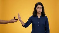 Young Hispanic businesswoman in navy shirt refusing cigarette offer with stop hand gesture against yellow background for anti-smoking health campaigns.