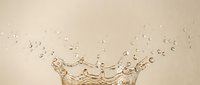 Water splash with droplets on beige background creating dynamic crown shape for beverage advertising and product photography applications.