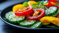 Fresh sliced cucumber, bell peppers and tomatoes on black plate with herbs and seasonings, close up view of colorful vegetable salad for healthy eating.