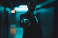 Silhouetted male figure pointing finger in dark corridor with dramatic cyan lighting and bokeh effects, creating mysterious and cinematic atmosphere.