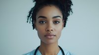 Young African American woman with natural curly hair and gentle expression looking directly at camera against light blue background in professional studio portrait.