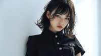 Young Asian woman with short wavy hair and bangs wearing elegant black outfit with gold buttons against white background, portraying confidence and style.