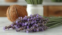 Fresh lavender sprigs with purple blooms on marble countertop beside coconut and jar of greenery, creating natural spa-like arrangement.