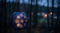 Decorative stained glass lantern with floral pattern hanging outdoors at dusk, creating warm ambient lighting for garden or patio decoration.