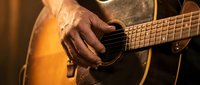 Close-up of mature male hands playing acoustic guitar with warm lighting, showcasing musical passion and skill for entertainment and hobby concepts.
