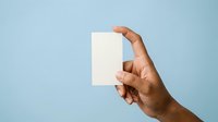 Male hand with medium skin tone holding blank white card against blue background, suitable for mockups, business presentations, and advertising campaigns.