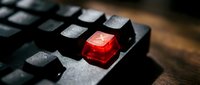 Close-up of black mechanical keyboard with single glowing red translucent keycap standing out among dark keys for gaming and typing concepts.