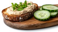 Fresh tuna spread on toasted dark bread slice garnished with parsley, served with cucumber rounds on wooden cutting board. Close up food photography.
