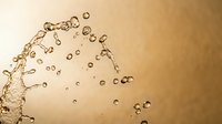 Water splash with droplets and bubbles on golden brown background creating dynamic liquid motion for beverage and refreshment concepts.