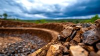 Dramatic close-up of eroded soil layers and rocks against stormy sky background shows environmental impact of land degradation and climate change effects on landscape.