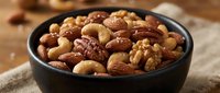Mixed nuts assortment in black bowl with almonds, walnuts, pecans and cashews on rustic wooden table for healthy snacking and cooking ingredients.
