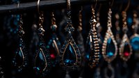 Elegant crystal teardrop pendants with blue gemstones and metallic details hanging in dark ambiance, creating luxurious jewelry display against blurred background.