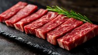 Fresh marbled beef slices arranged in row on black stone surface with rosemary sprig, raw premium meat cuts showing rich texture and marbling pattern.