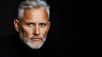 Senior man with gray hair and beard wearing black turtleneck against dark background, suitable for corporate portraits, business profiles, and professional headshots.