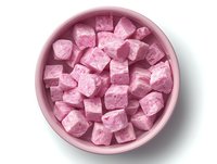 Pink marshmallow cubes in ceramic bowl on white background, top view. Sweet homemade confectionery dessert with powdered sugar coating isolated.