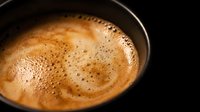Fresh brewed coffee with creamy foam and bubbles in black cup on dark background for morning beverage and cafe menu designs.
