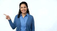 Smiling young Hispanic businesswoman in blue shirt pointing left with finger gesture on white background for presentations and marketing materials.