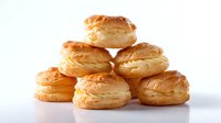 Fresh baked puff pastry shells stacked in pyramid formation on white background, flaky golden layers with delicate texture, ready for filling and serving.