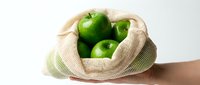 Fresh green apples in a reusable mesh cotton bag held by hand, promoting eco-friendly shopping and zero waste sustainable lifestyle.