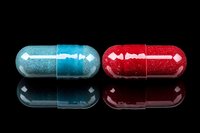 Red and blue medical capsules with glitter effect on black reflective surface, isolated pharmaceutical pills with mirror reflection for healthcare concept.