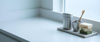 Minimalist bathroom accessories set with soap dispenser, cup and soap on marble tray near bathtub edge, clean modern spa-like interior design for relaxation.