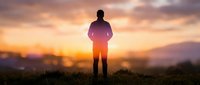 Male silhouette standing on hill during golden hour sunrise with dramatic orange and pink sky clouds creating inspirational outdoor scene for motivation concepts.