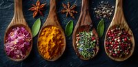 Colorful spices and herbs in wooden spoons on dark background - turmeric, rose petals, peppercorns and rosemary arranged in rustic culinary composition.