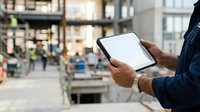 Man holding tablet with blank screen in urban street setting, suitable for app mockups and technology marketing.