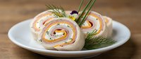 Pinwheel sandwiches with smoked salmon, cream cheese, and fresh dill garnish on white plate for catering, appetizers, and food service.